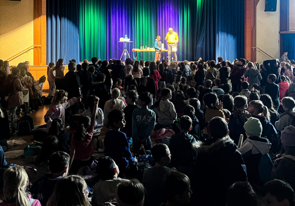 Kinder sitzen vor Bühne und schauen Chemie-Show an